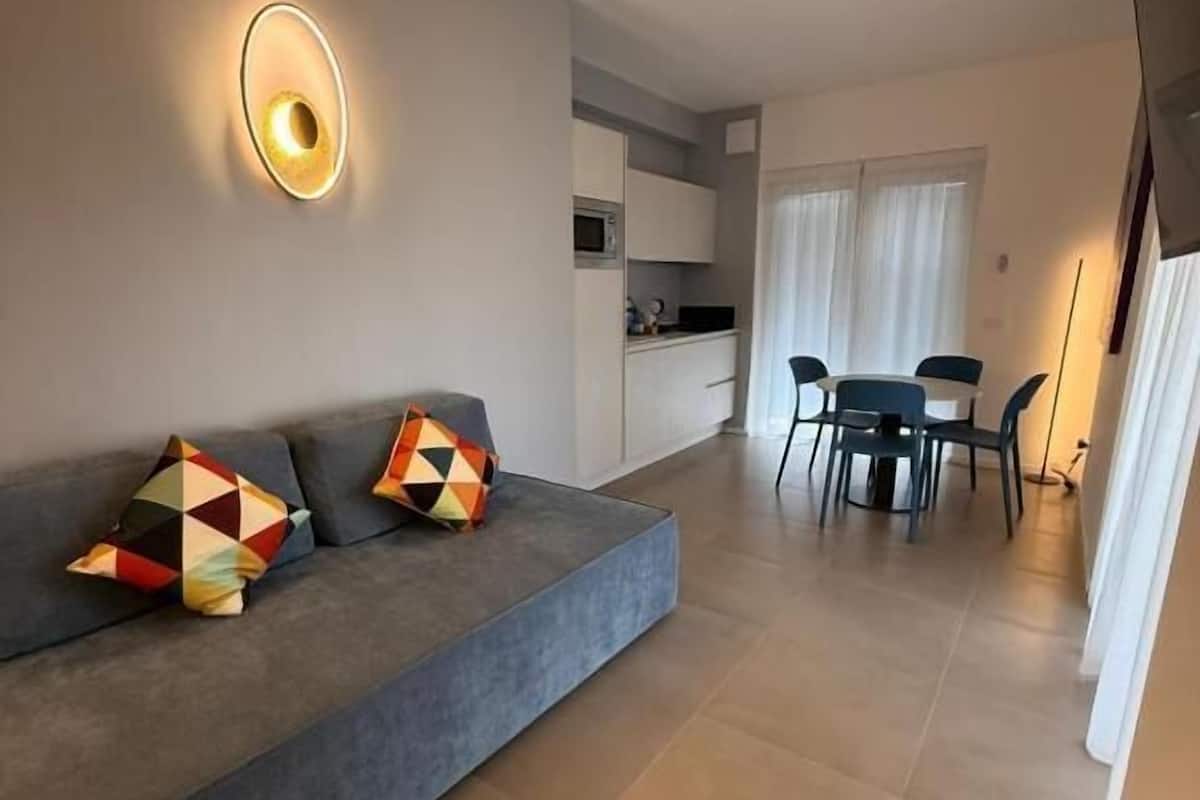 A modern living room with a sofa, a dining table, and a kitchen area in the background.