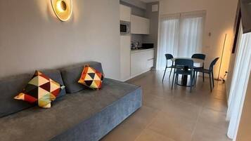 A modern living room with a sofa, a dining table, and a kitchen area in the background.