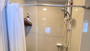 Zona de ducha con puerta de vidrio, ducha de mano y llave empotrada.