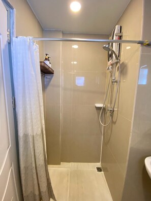 Zona de ducha con puerta de vidrio, ducha de mano y llave empotrada.