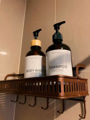Two bottles of body wash and shampoo on a metal shelf. - Linlaada Property Kamala (Kamala)