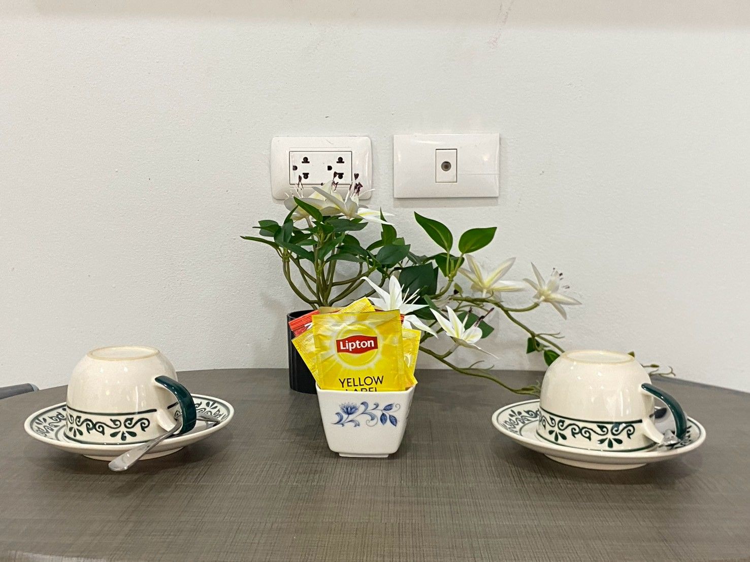 A table with two teacups and a vase with flowers and Lipton tea bags.