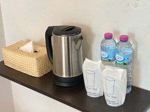 A kitchen counter with a woven tissue box, a stainless steel kettle, two water bottles, and two glass tumblers.