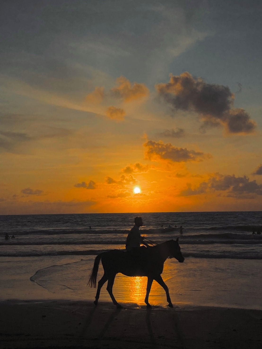 A silhouette of a person riding a horse on a beach at sunset.