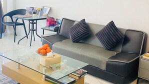 Una sala moderna con una mesa de centro de vidrio, un sofá gris con cojines negros, una obra de arte en la pared y una zona de comedor con una silla y una mesa.