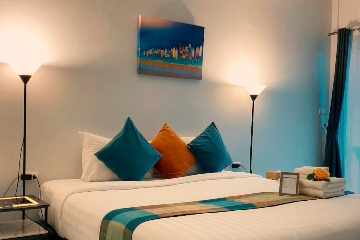 A hotel room with a bed, two bedside lamps, a painting on the wall, and a nightstand with a lamp and a device.
