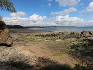 A coastal landscape with rocky terrain, a sandy beach, and a view of the sea under a partly cloudy sky. - Sandpiper (Narberth)