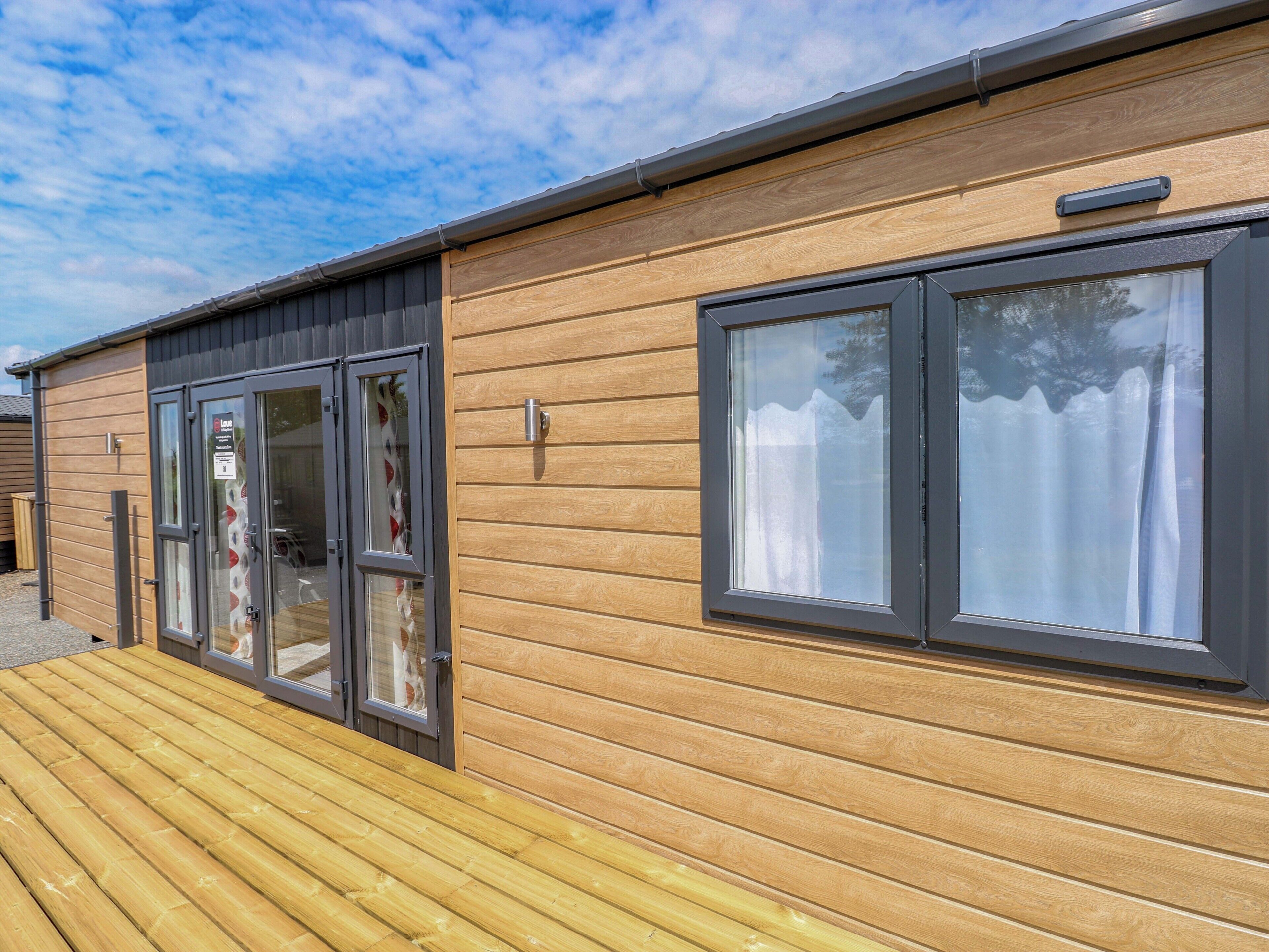 A wooden cabin with a deck, a sliding glass door, and a window with curtains.