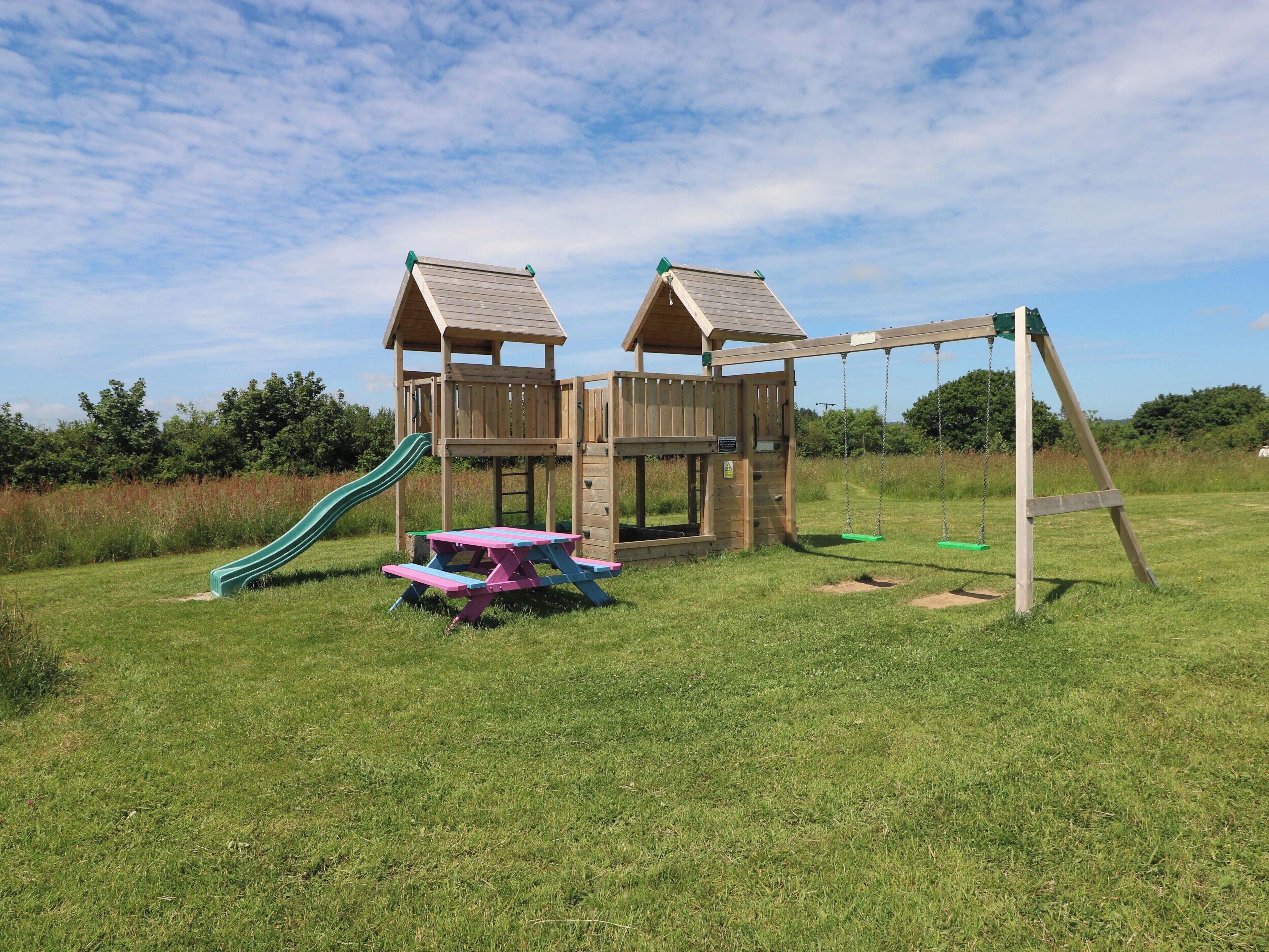 A wooden play structure with a slide and swings, surrounded by grass.