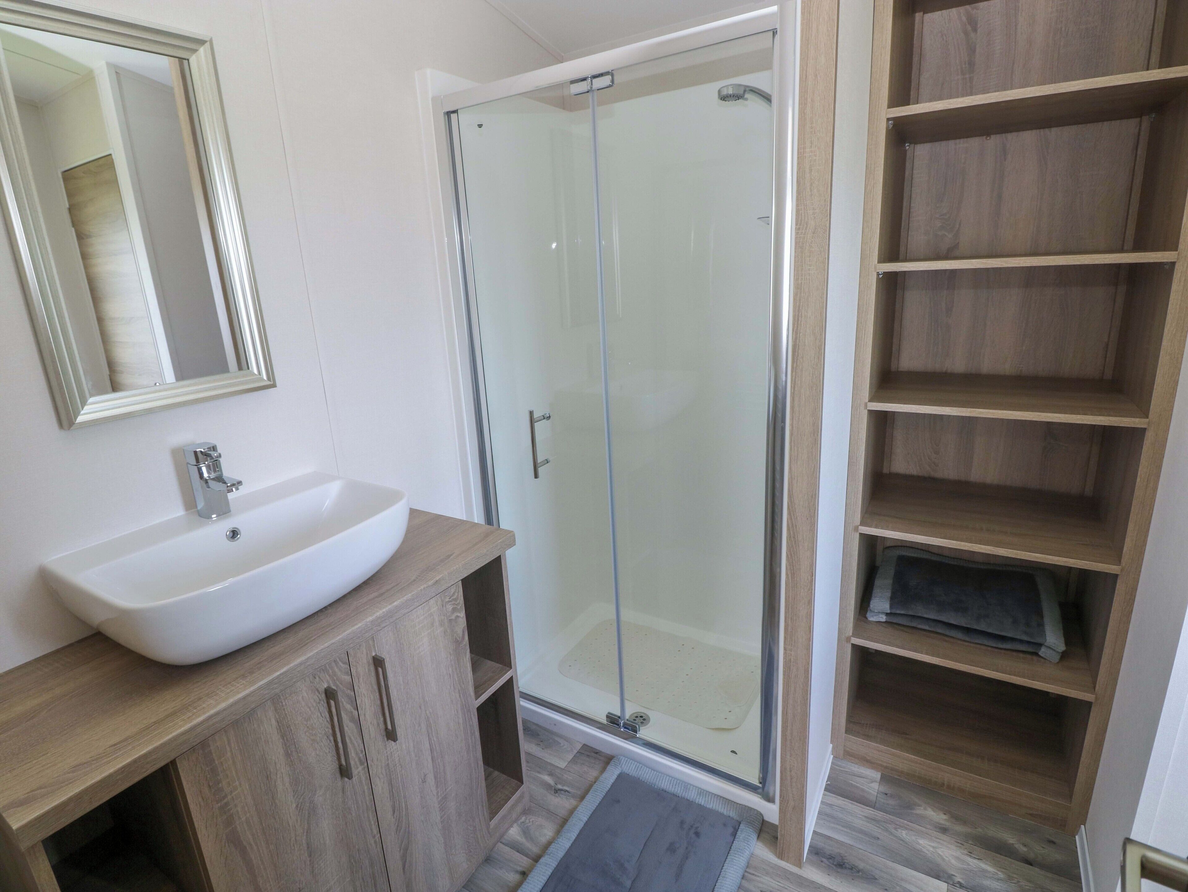 A bathroom with a white sink, a glass shower enclosure, and wooden shelving.