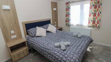 Un dormitorio con cama, mesitas de noche, una ventana con cortinas y un radiador.