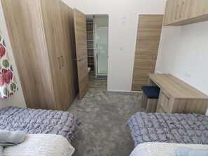A bedroom with two beds, a wardrobe, a desk, and a bathroom. - Sandpiper (Narberth)