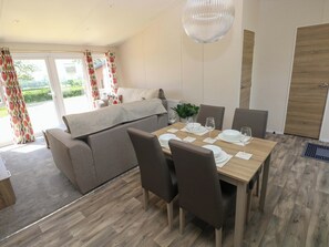 A dining area with a wooden table set for six, a sofa, and a large window with curtains. - Sandpiper (Narberth)