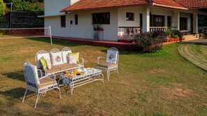 Ein zweistöckiges Haus mit rotem Ziegeldach, einer überdachten Veranda und einem Rasen mit Gartenmöbeln.