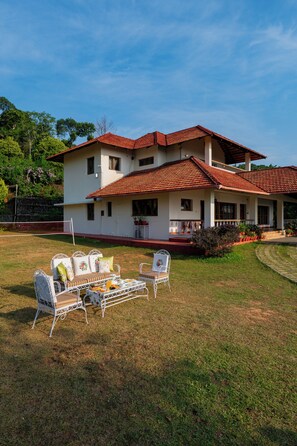 A two-story house with a red-tiled roof, a covered porch, and a lawn with outdoor furniture.