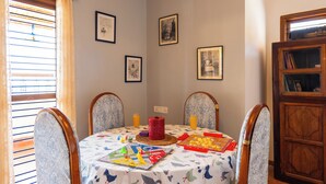 A dining area with a table set for four, featuring a patterned tablecloth, chairs with floral upholstery, and framed pictures on the wall.