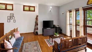 Ein Wohnzimmer mit einer Couch, einem Fernseher, einem Schrank und einem Fenster mit Vorhängen.