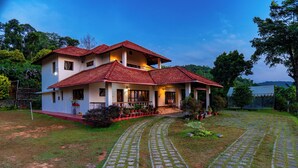 A two-story house with a red-tiled roof, a paved driveway, and a well-maintained garden.