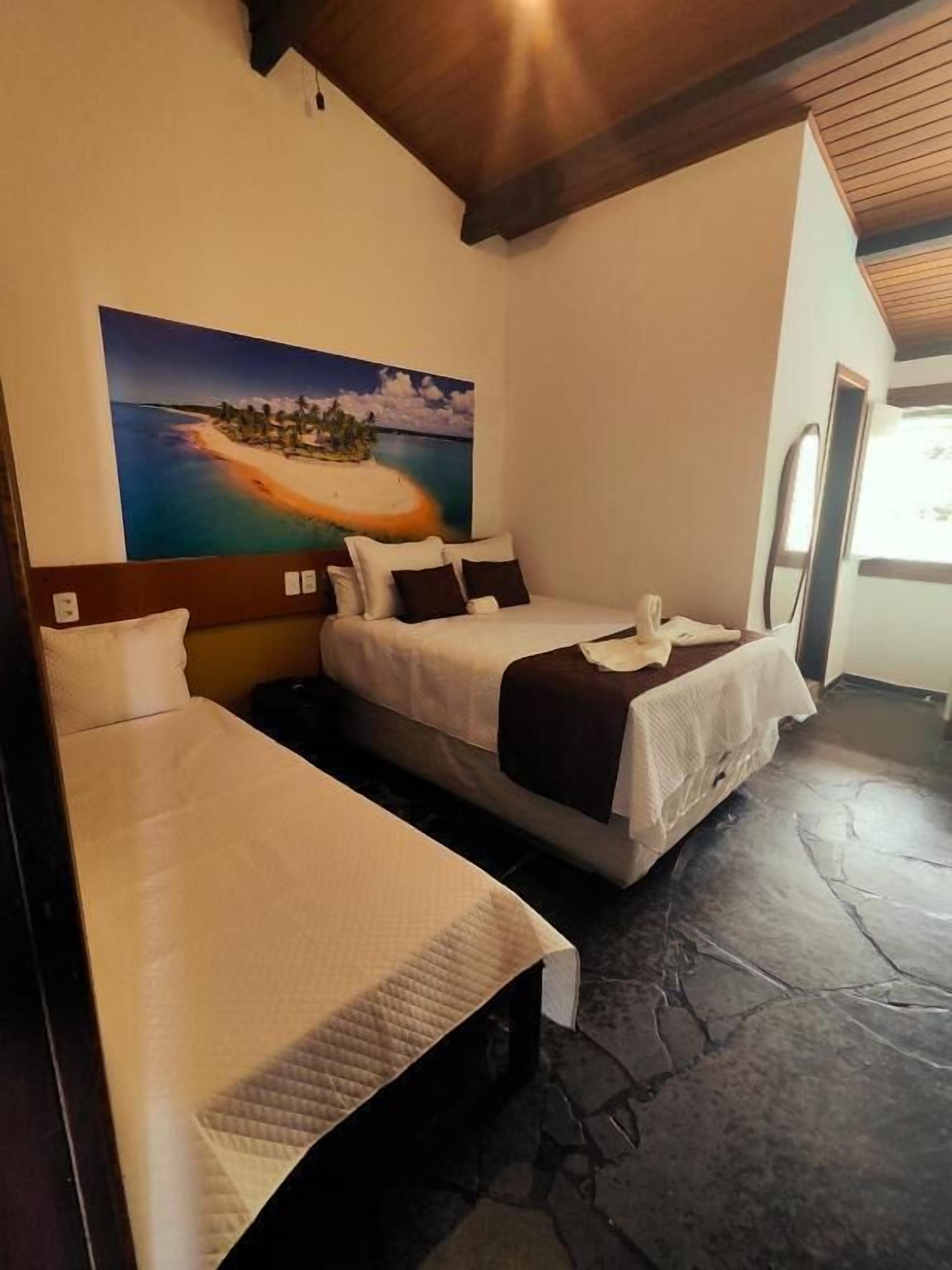A room with two beds, a painting of a tropical island, and a stone floor.