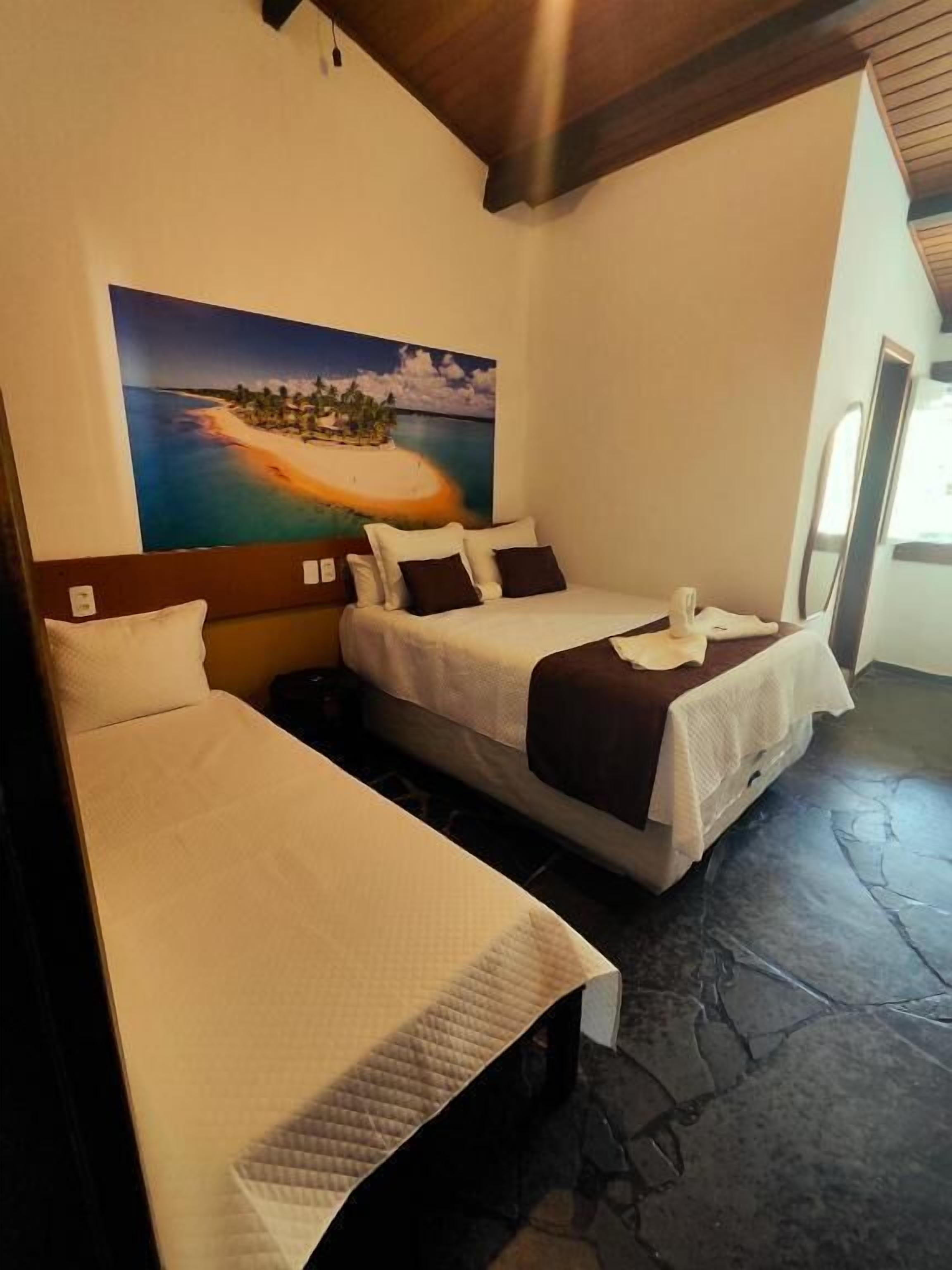 Una habitación de hotel con dos camas, un cuadro de una playa y suelo de piedra.