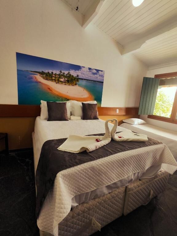A hotel room with a bed, a painting of a beach, a window, and a nightstand.