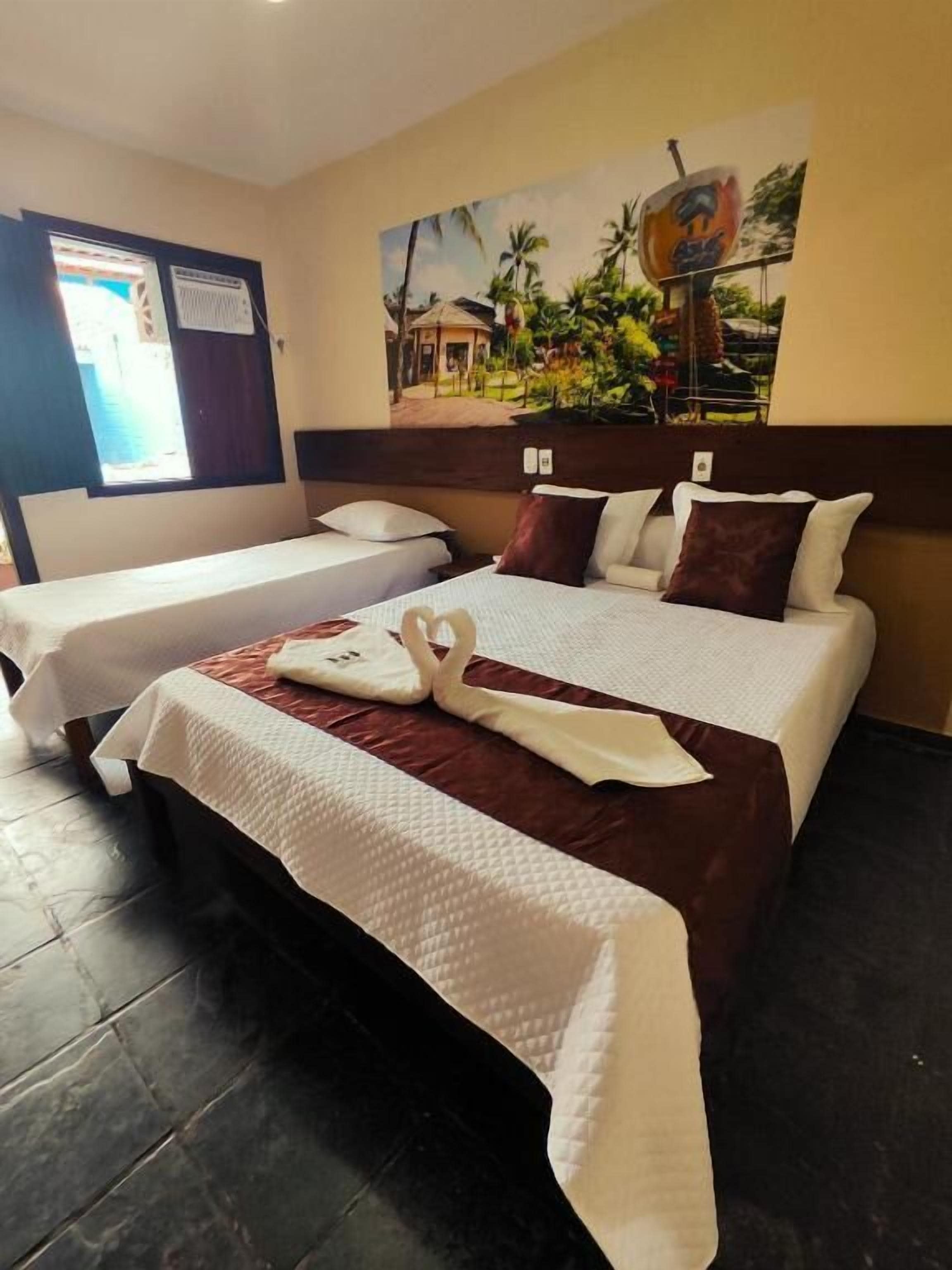 A hotel room with two beds, a painting on the wall, and a window with a view.