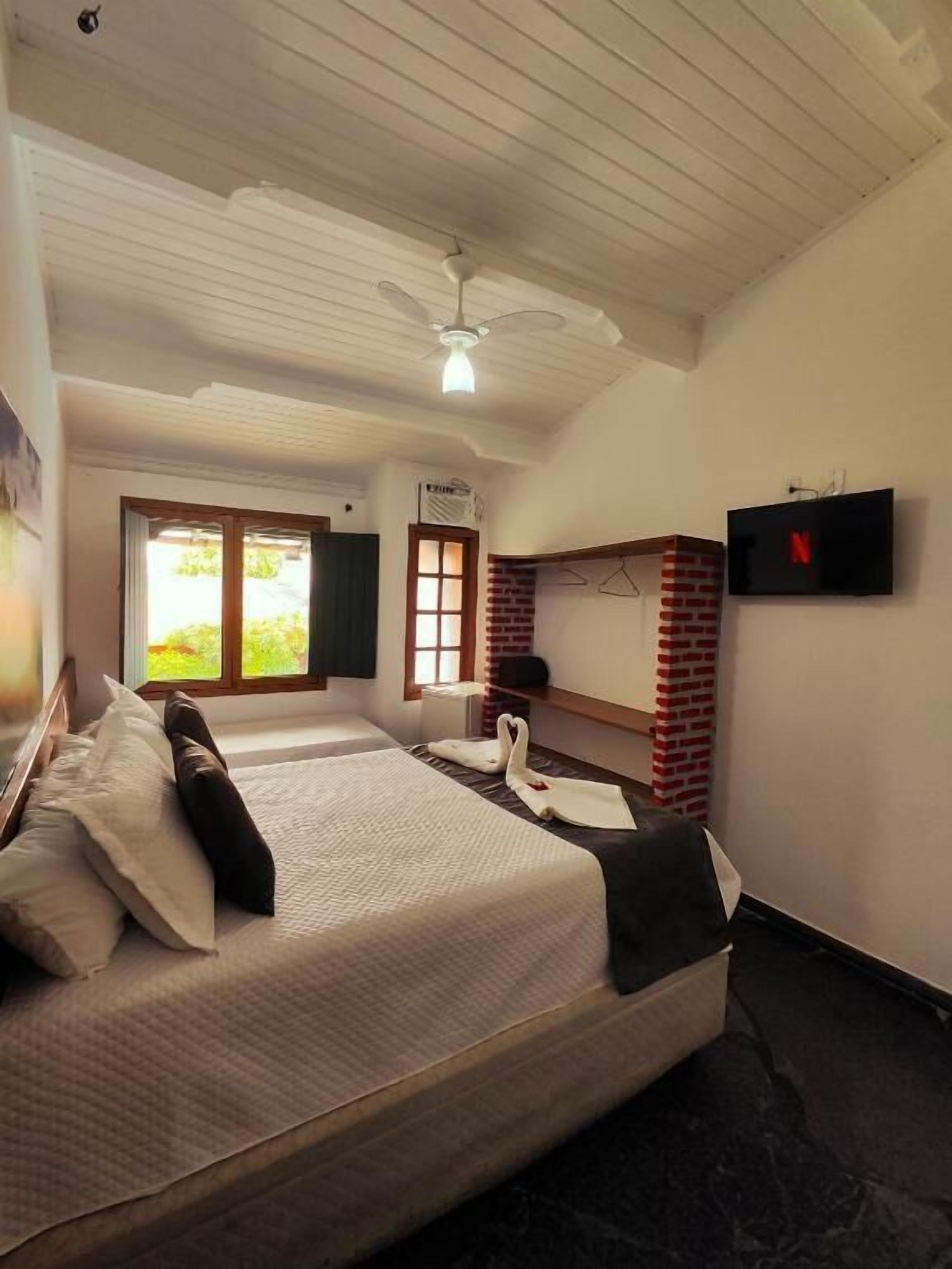 A hotel room with two beds, a TV, a window with a view, and a ceiling fan.