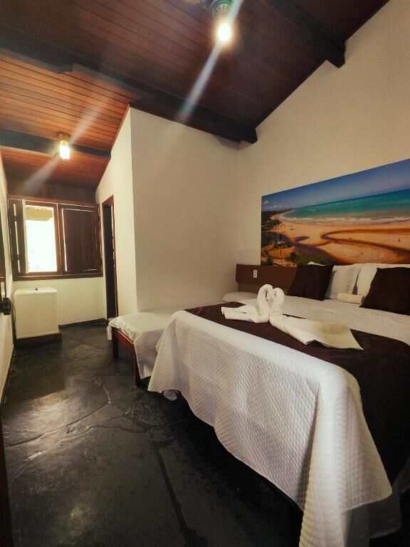 A bedroom with a bed, a painting of a beach, a wooden ceiling, and a window.