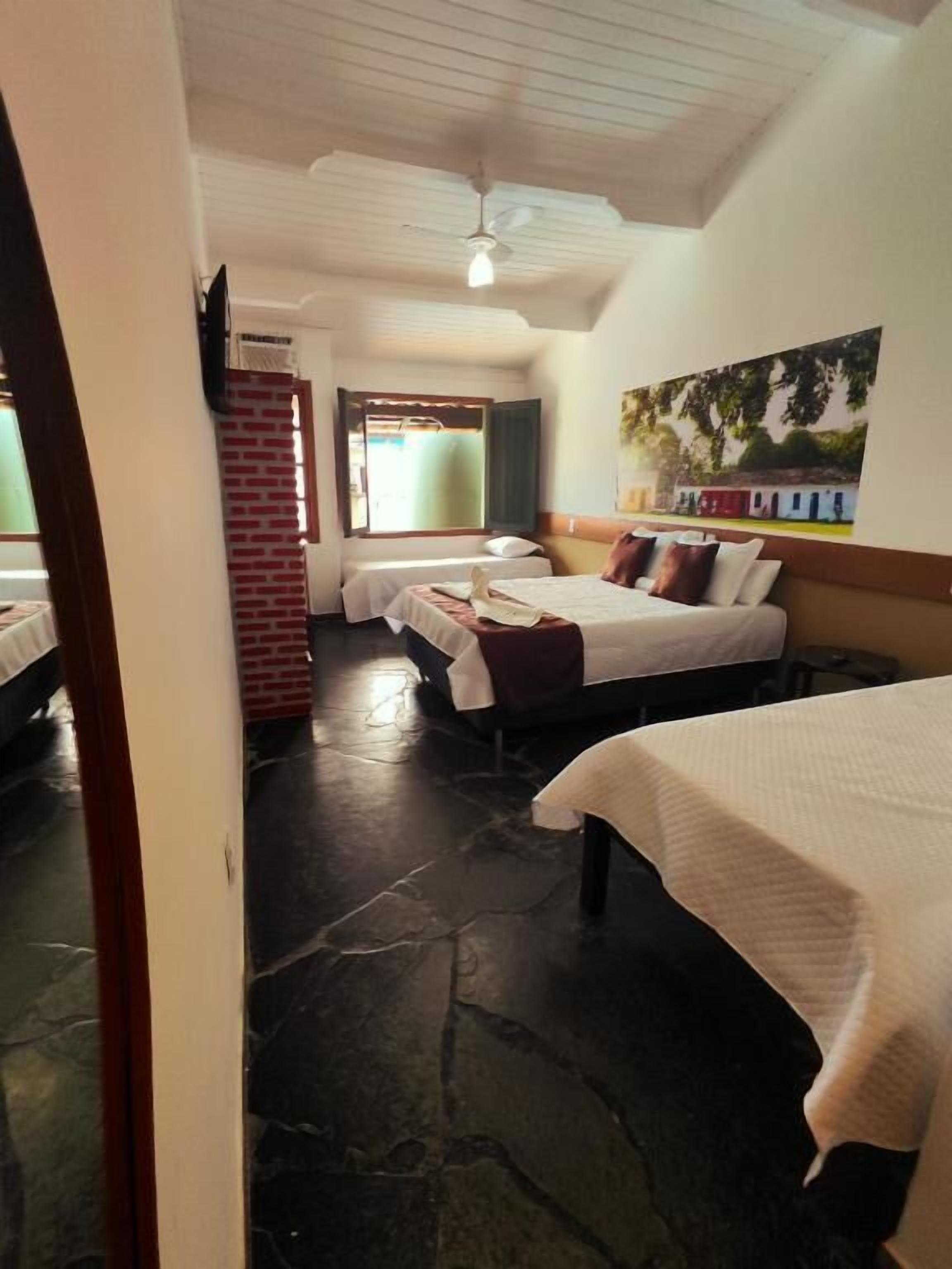 A hotel room with two beds, a brick wall, a ceiling fan, and a painting on the wall.