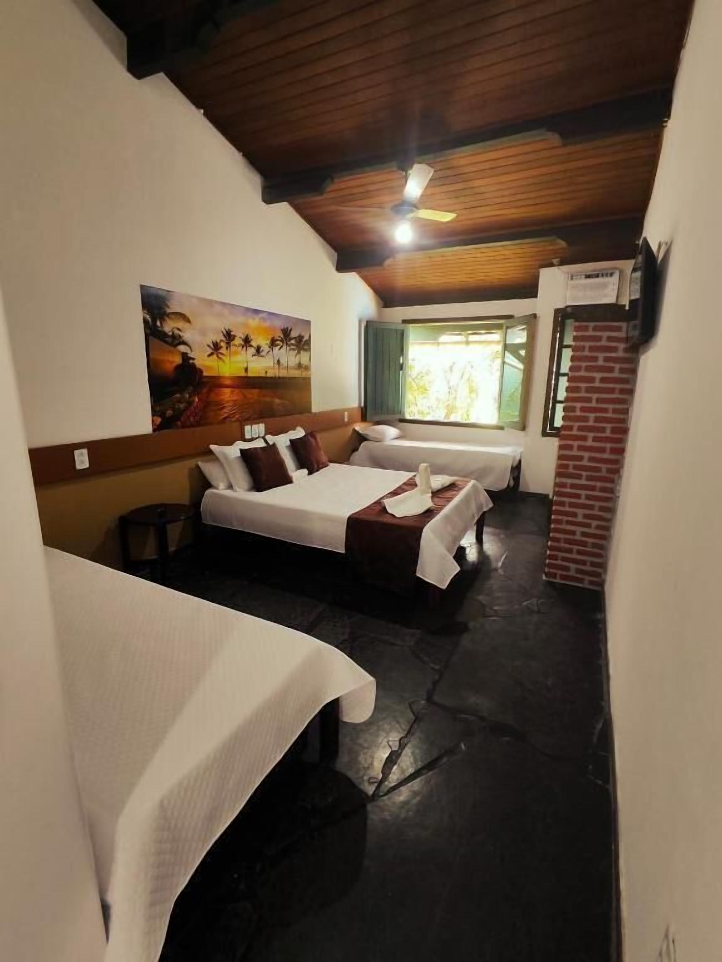 A room with two beds, a painting on the wall, a ceiling fan, and a window with a view.