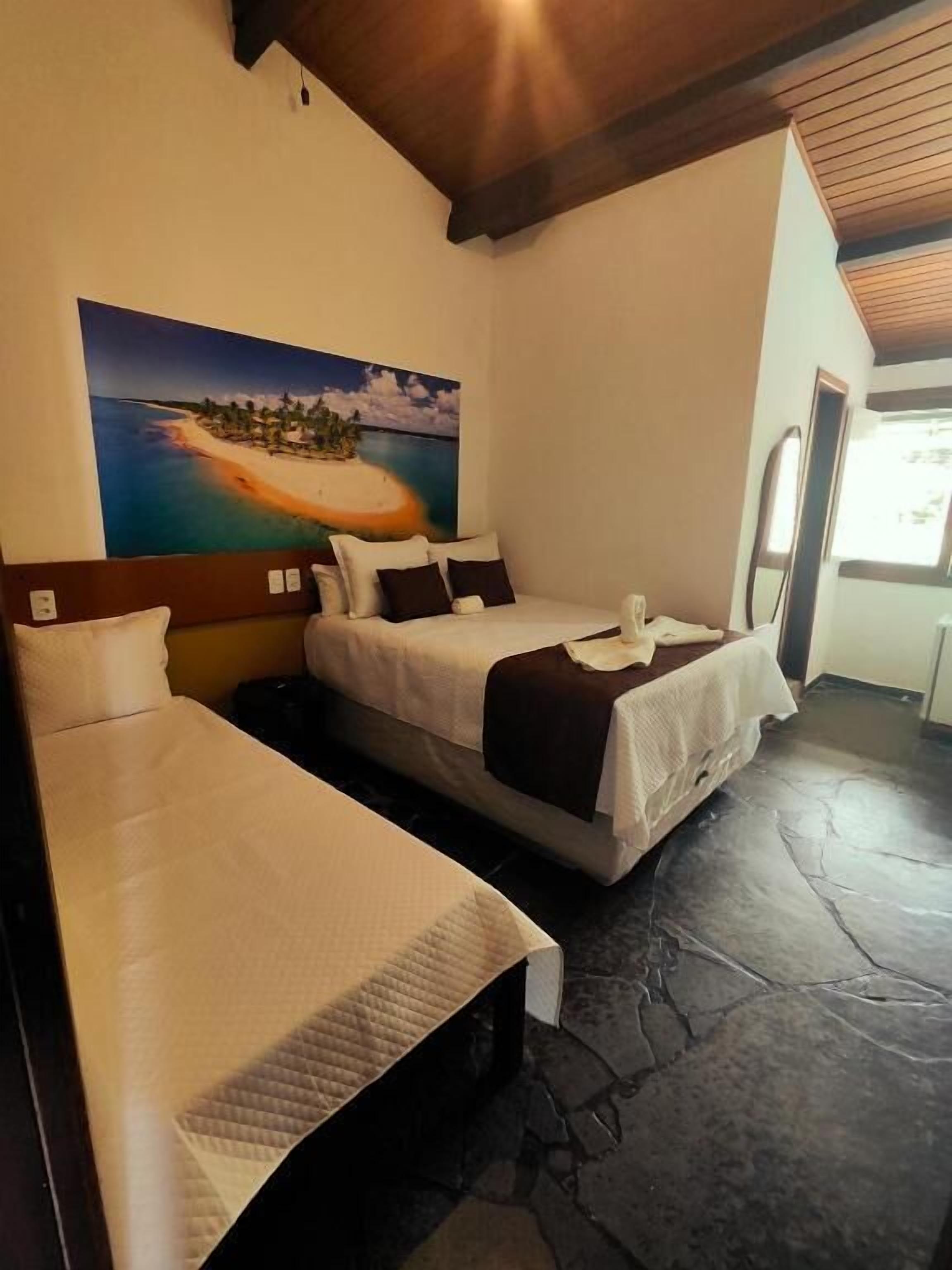 Una habitación con dos camas, un cuadro de una playa, suelo de piedra y techo de madera.