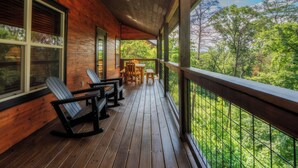 A wooden deck with chairs and a table, overlooking a forested area. - SmokySplashRetreat: Pool, Wifi, Hot Tub, Game Room, Partial Mtn Views (Sevierville)