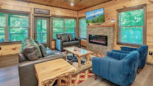 A cozy cabin interior with a fireplace, comfortable seating, and large windows. - SmokySplashRetreat: Pool, Wifi, Hot Tub, Game Room, Partial Mtn Views (Sevierville)