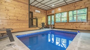An indoor swimming pool with wooden walls, a bench, and a chair. - SmokySplashRetreat: Pool, Wifi, Hot Tub, Game Room, Partial Mtn Views (Sevierville)