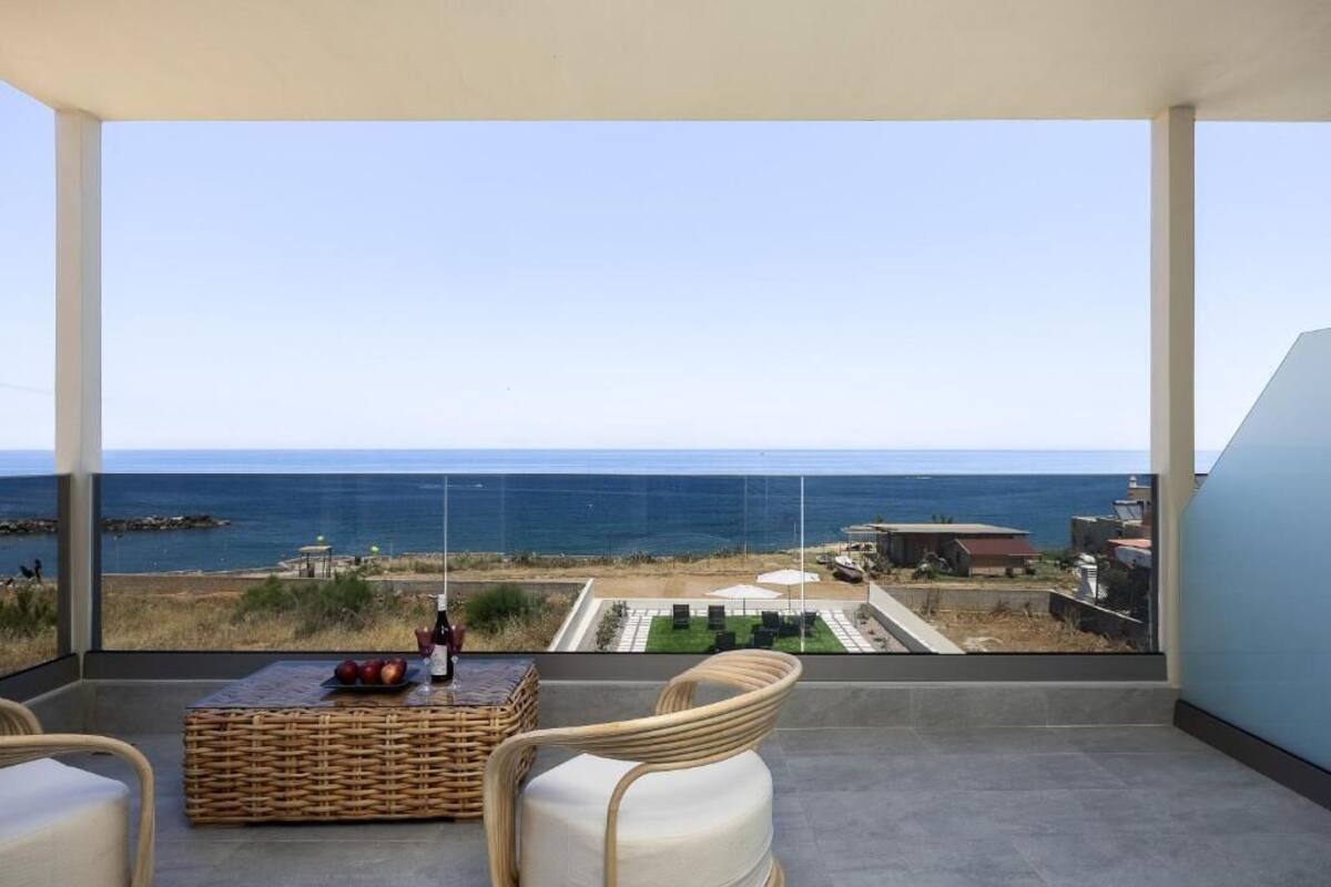 A balcony with a view of the ocean, wicker furniture, and a table with fruits and a bottle.