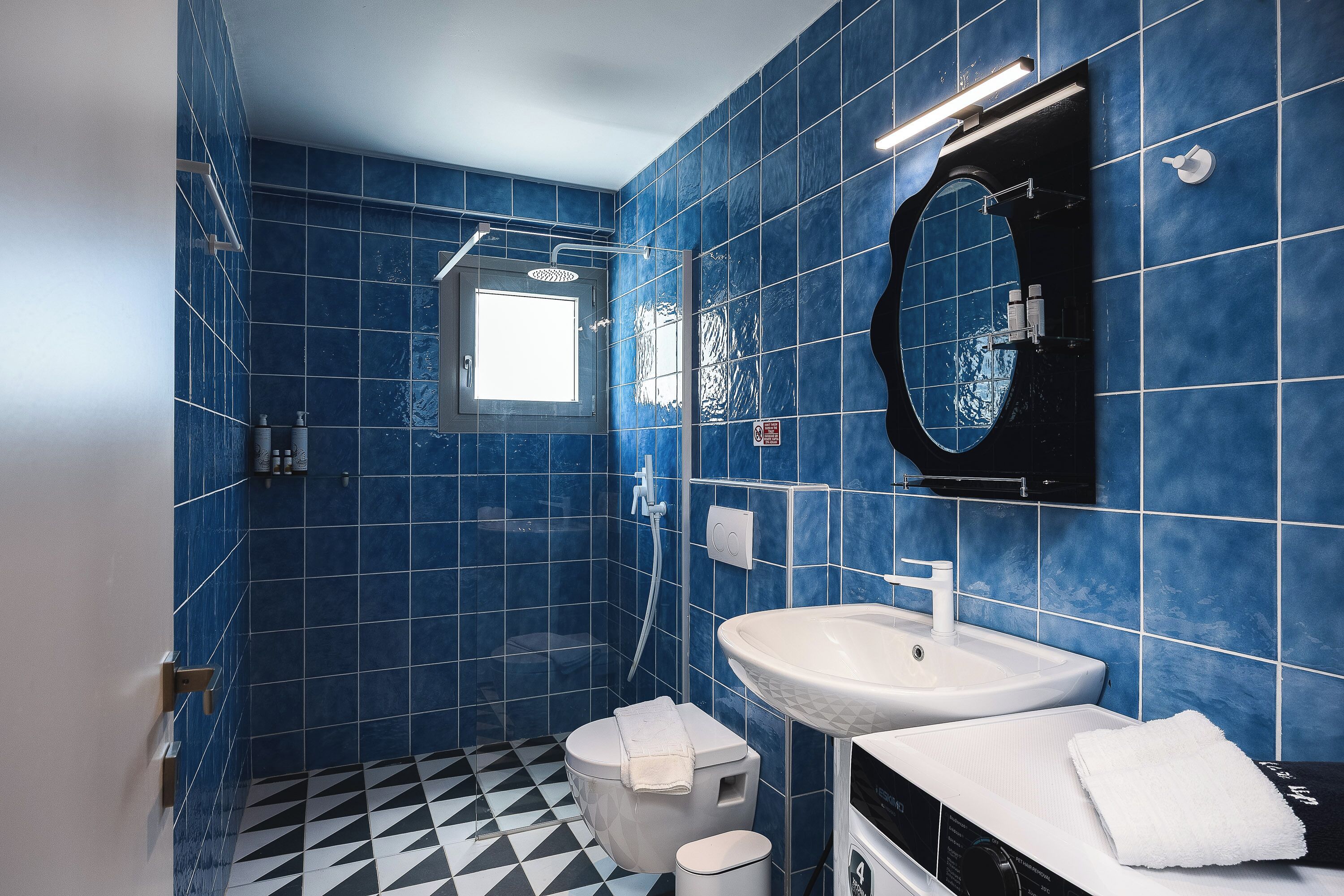 A bathroom with blue tiles, a white sink, a toilet, and a shower.