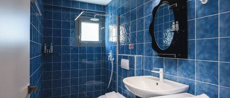 A bathroom with blue tiles, a white sink, a toilet, and a shower.