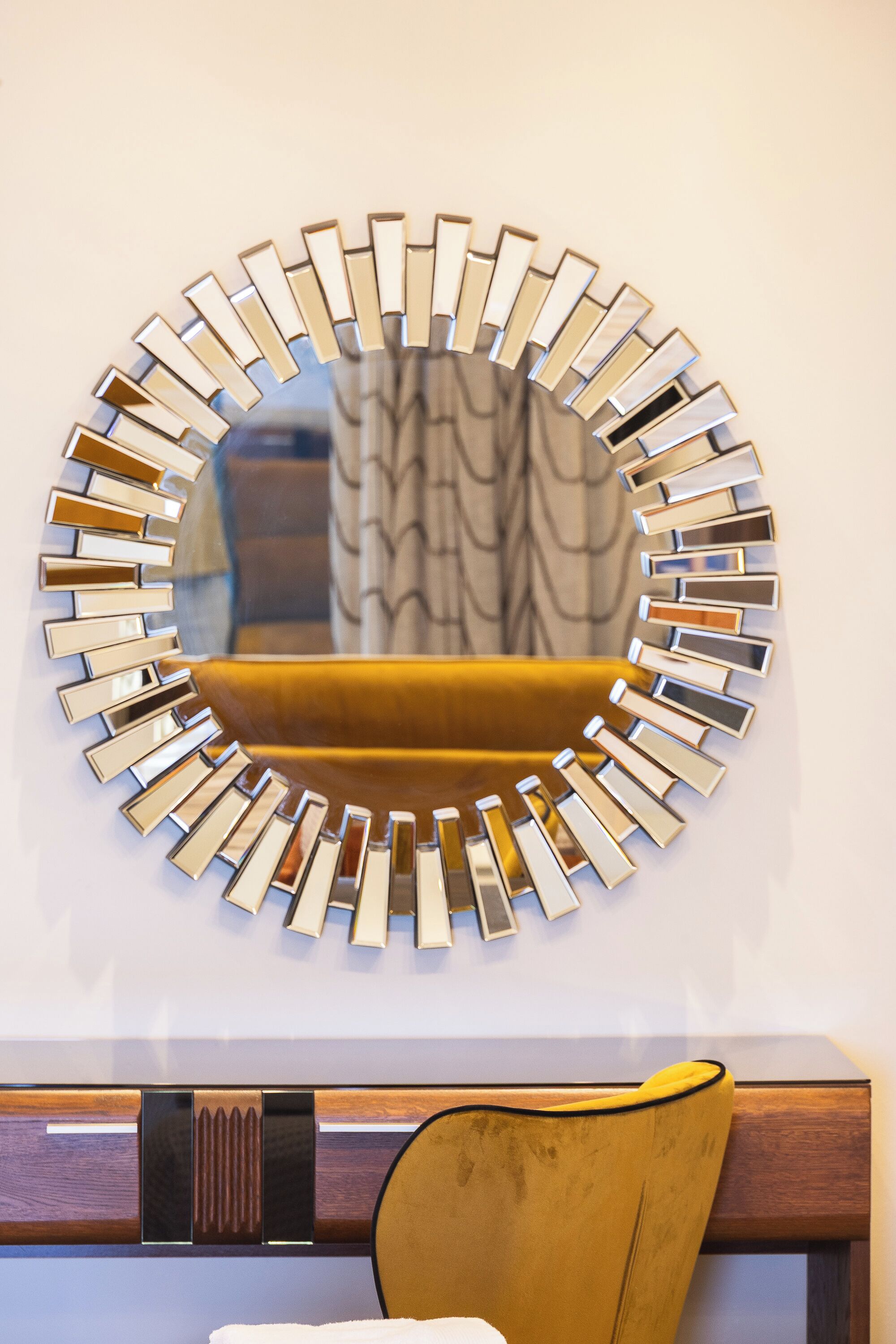 A circular mirror with a metallic frame, a yellow upholstered chair, and a wooden headboard.