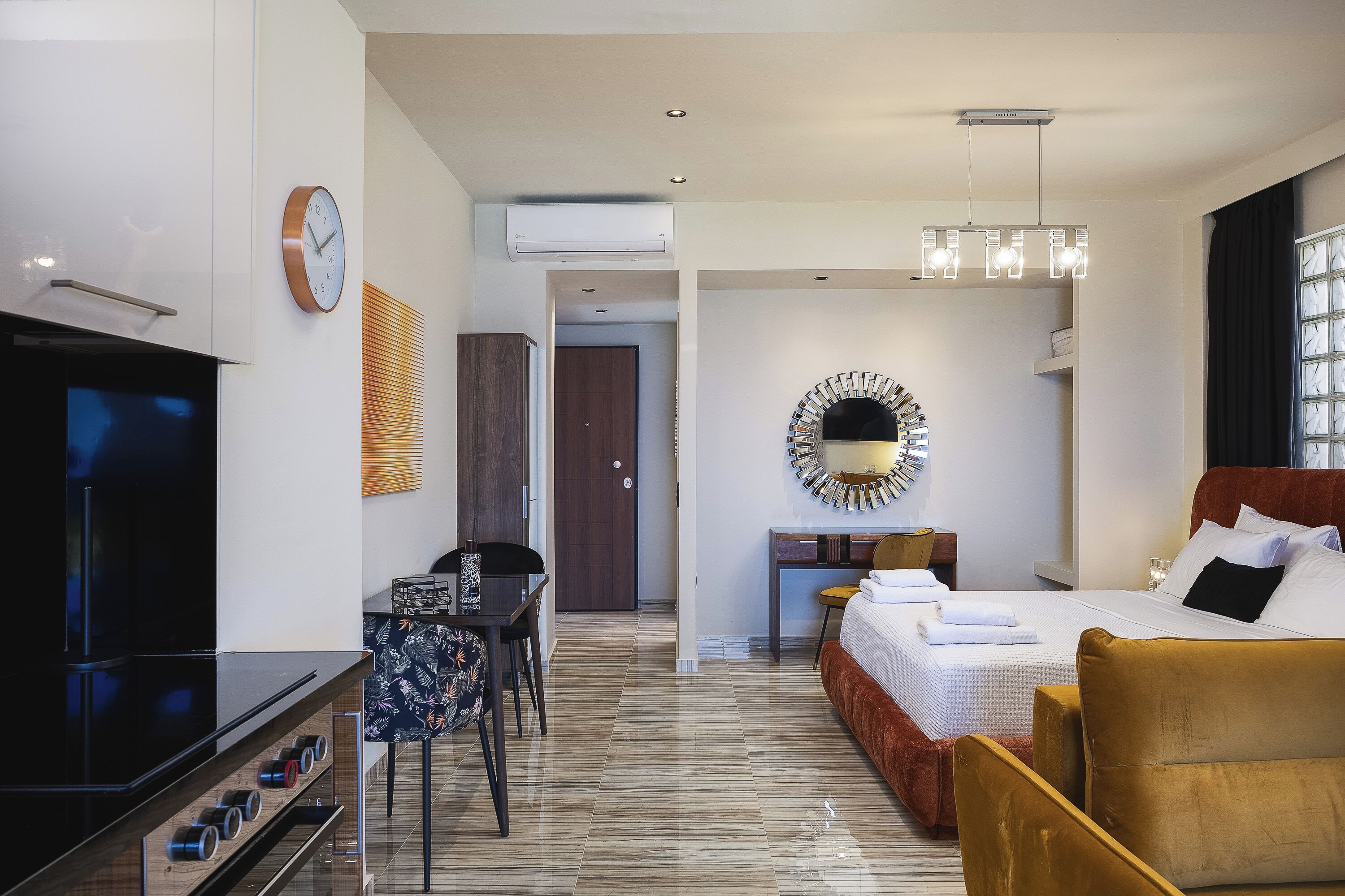 Una habitación de hotel moderna con televisor de pantalla plana, zona de comedor, cama con cabecera y un espejo grande.