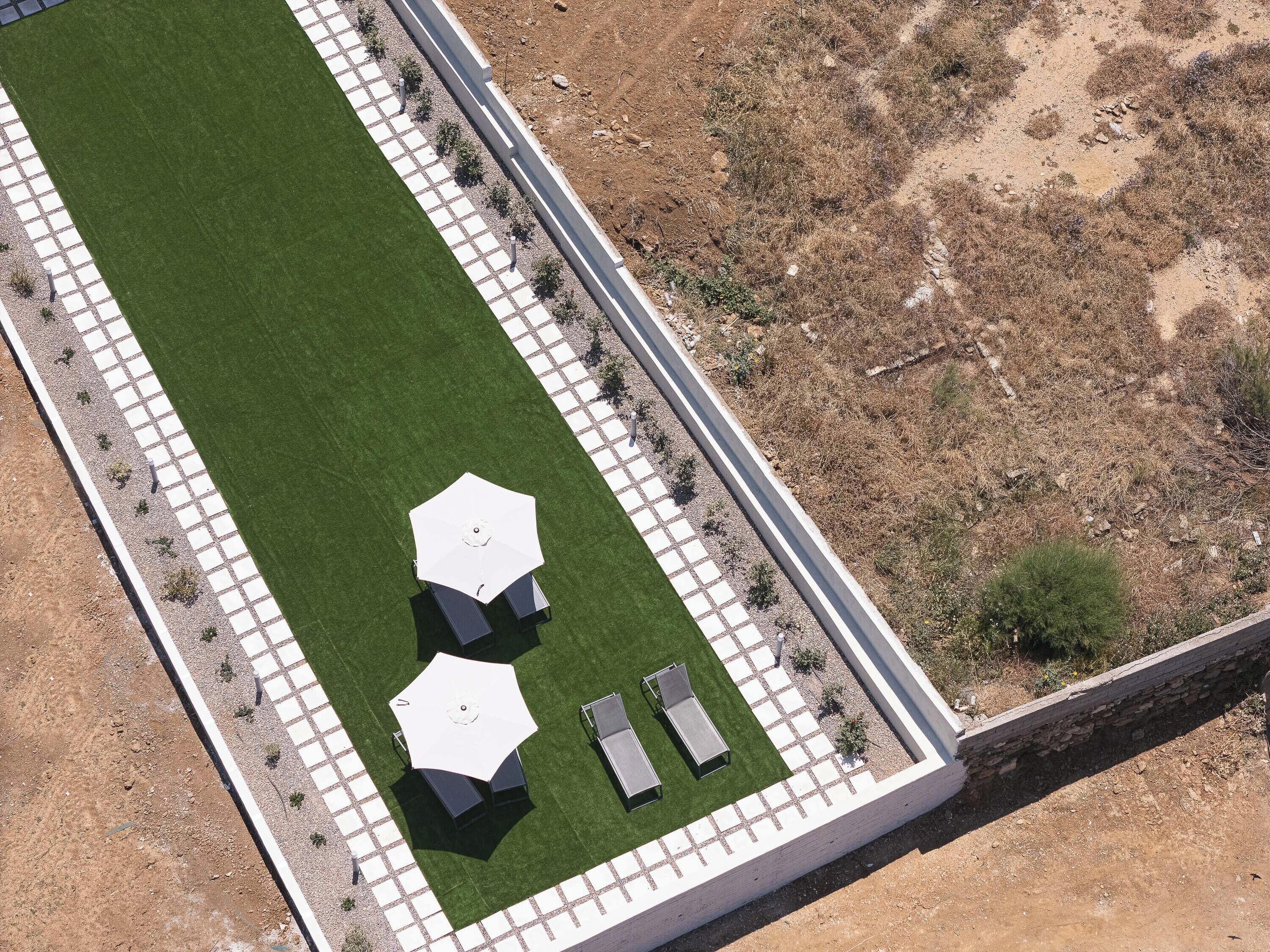 An aerial view of a landscaped area with a paved walkway, a grassy lawn, and outdoor seating with umbrellas.