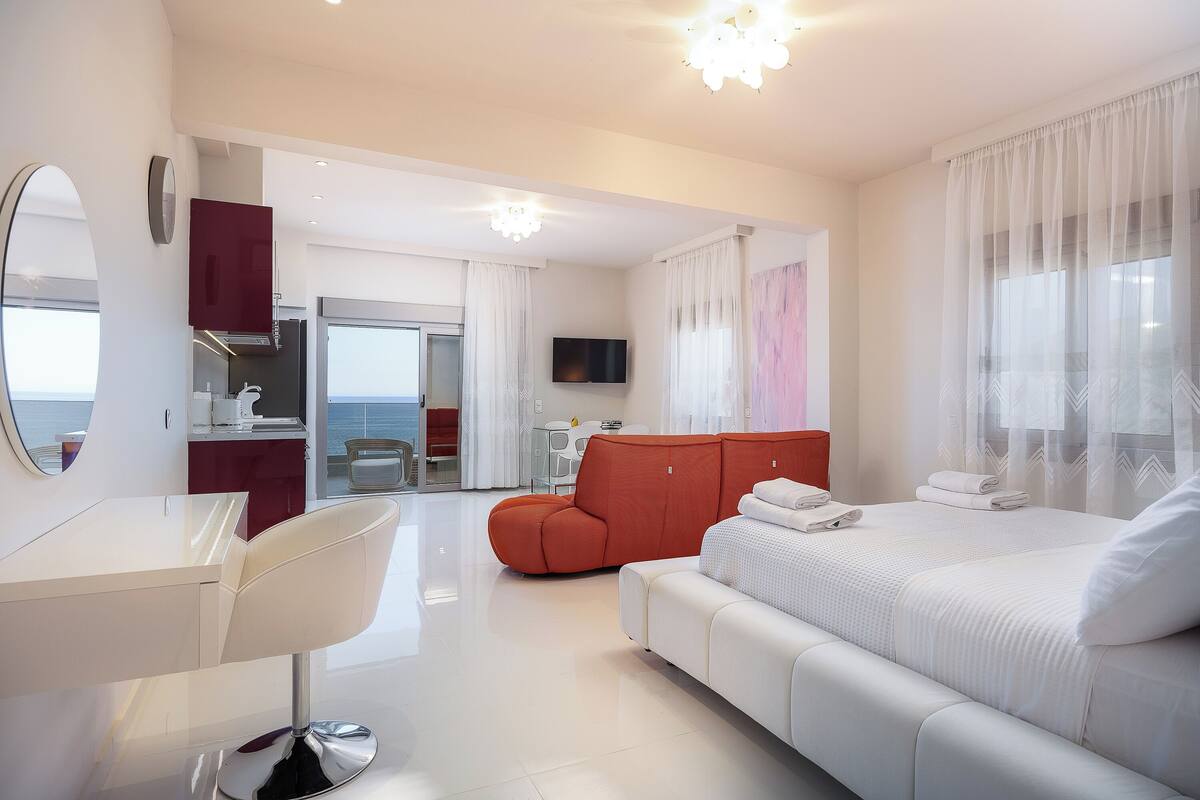 A modern hotel room with a bed, a sofa, a TV, and a bathroom.