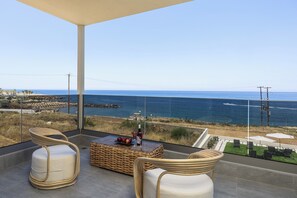 Ein Balkon mit Korbstühlen, einem Glastisch mit Obst und einer Flasche sowie Meer- und Strandblick.