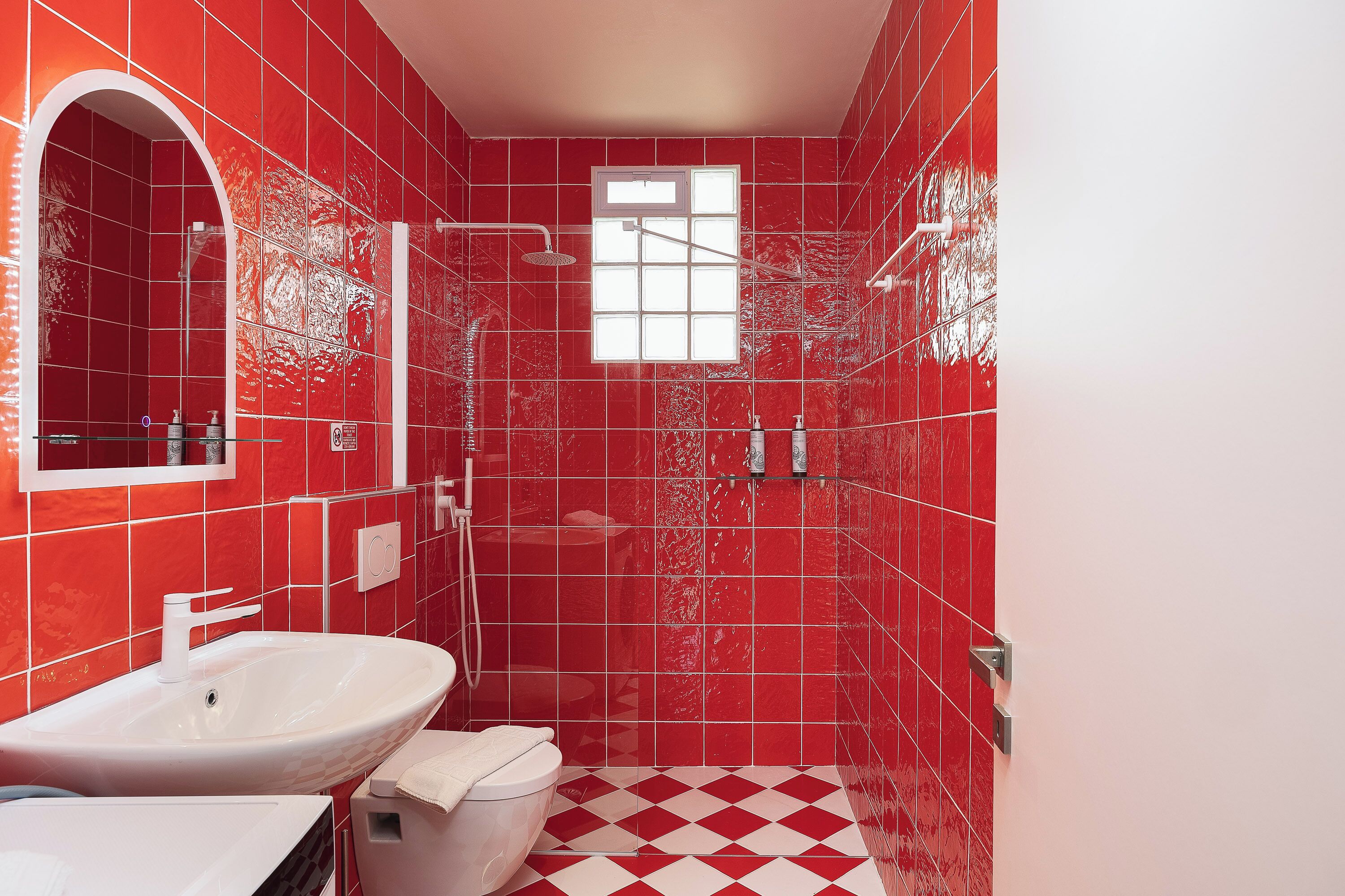 A bathroom with red tiles, a white sink, and a shower area.