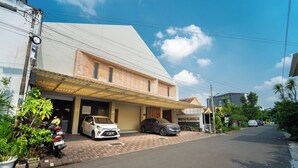 A residential street with two parked cars, a covered carport, and a building with a tiled roof. - Tempuran Suites By ARBA (Sleman)