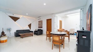 A modern living room with a sofa, a dining table with chairs, a TV, and a fan. - Tempuran Suites By ARBA (Sleman)