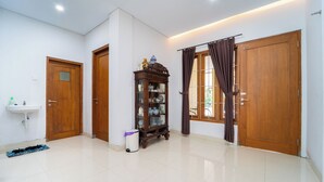 A room with a white tiled floor, a wooden door, a cabinet with glass doors, a sink, and a window with curtains. - Tempuran Suites By ARBA (Sleman)