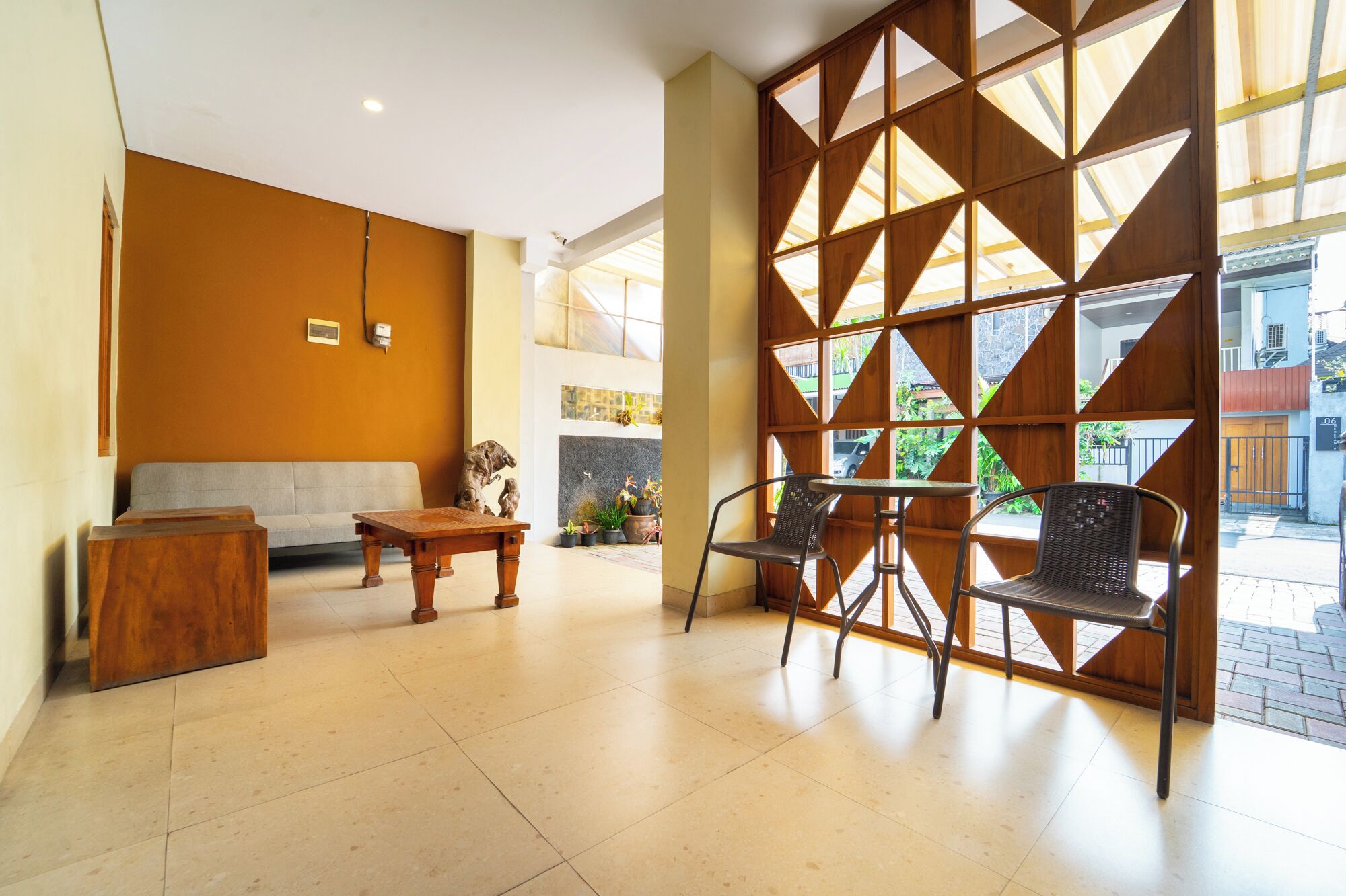 Uma área de recepção com sofá, mesa de madeira, cadeiras e uma parede decorativa com padrões geométricos.