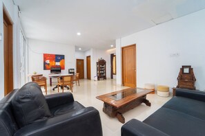 Uma sala de estar com sofá, mesa de centro, mesa de jantar com cadeiras, estante e televisão.