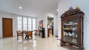 A spacious room with a wooden cabinet filled with decorative items, a dining area with chairs and a table, and a kitchen visible through an open doorway. - Tempuran Suites By ARBA (Sleman)