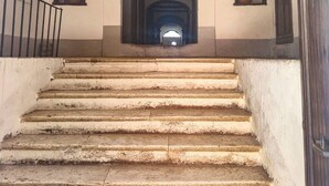 A staircase leading to an arched doorway, with a metal railing on the left and a door on the right.
